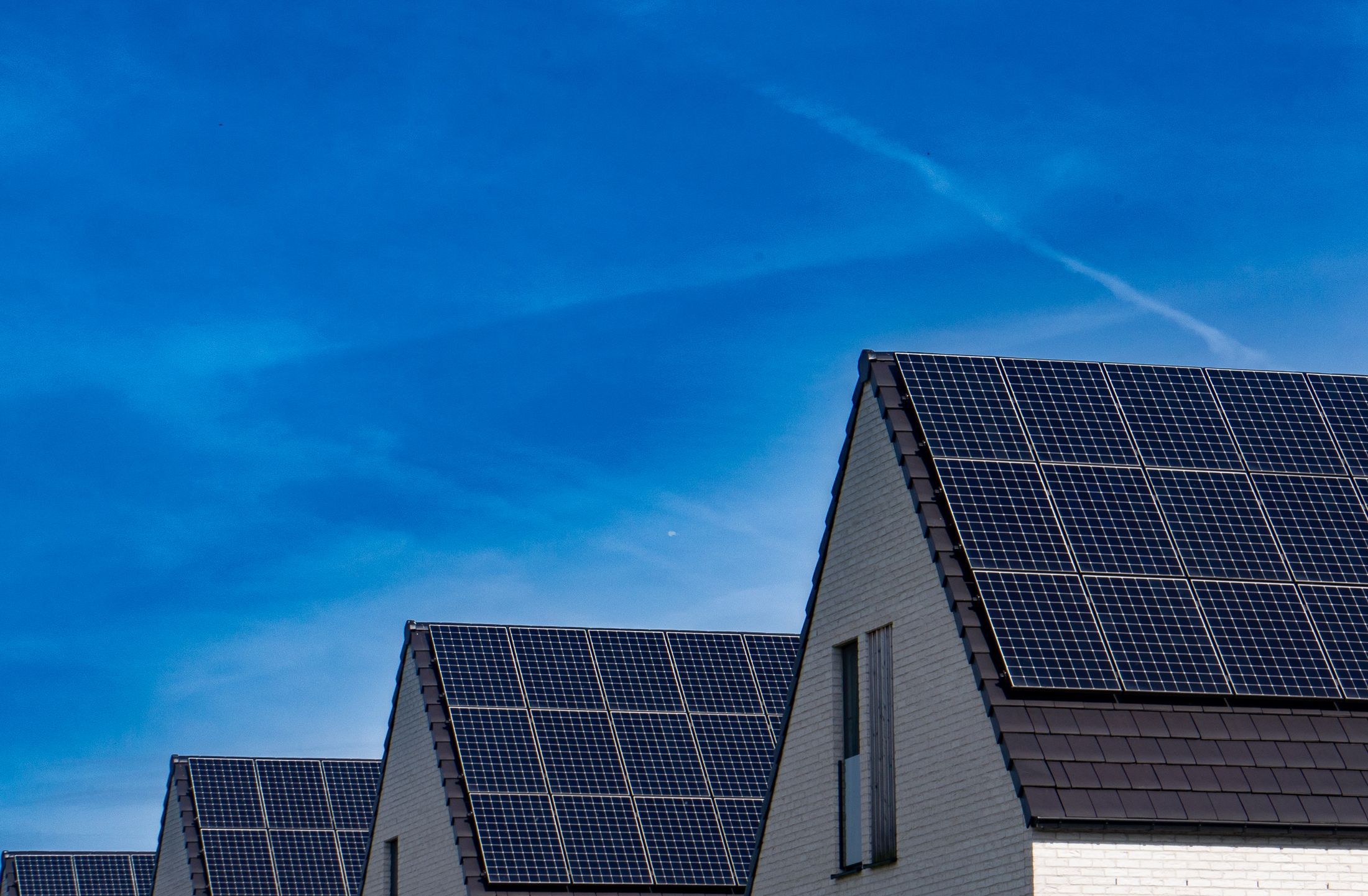 Maisons neuves aux toits sombres couverts de modules photovoltaïques, ciel bleu